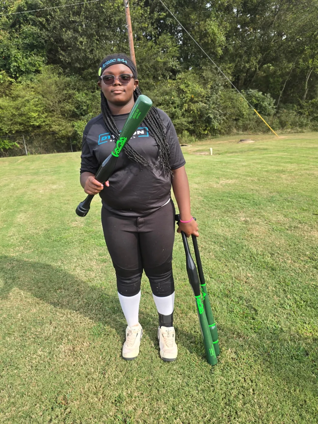 Softball player on a grass field holding green training bats