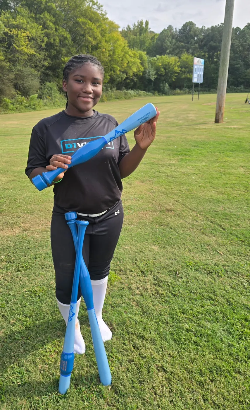 Softball player on a grass field holding blue training bats